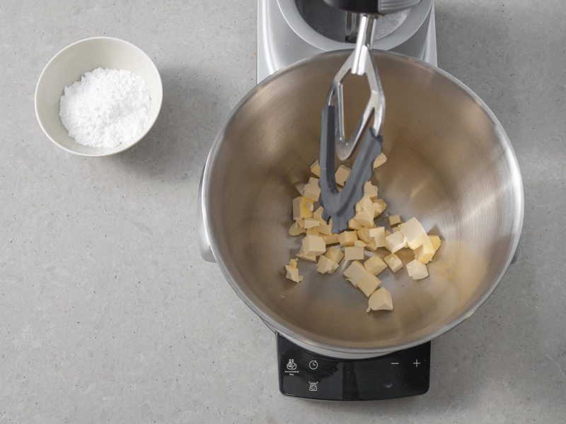 Margaryna wegańska w misie robota kuchennego bosch. Obok cukier puder w miseczce.
