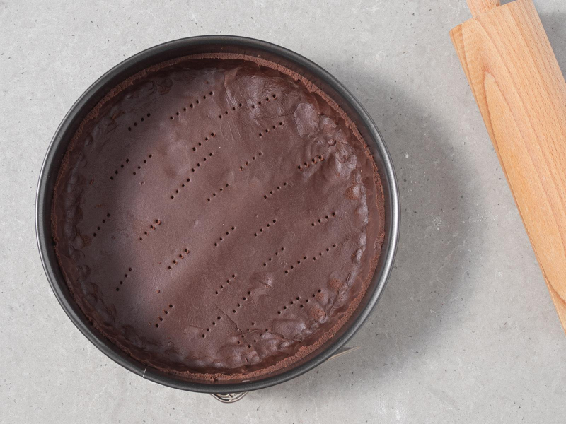 Wegański czekoladowy kruchy spód do tarty wyłożony w tortownicy.