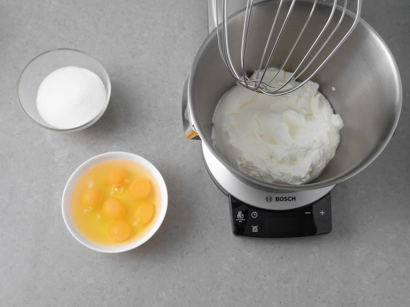 Twaróg w misie miksera kuchennego. Obok w miseczce cukier i jajka.