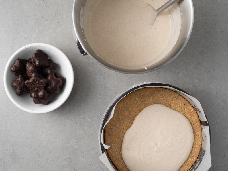 Nakładanie masy serowej na spód ciasteczkowy. Obok w misie pierniczki.