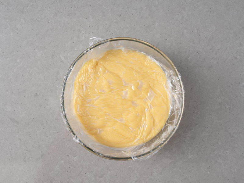 W szklanej misie ugotowany budyń, przykryty folią spożywczą.