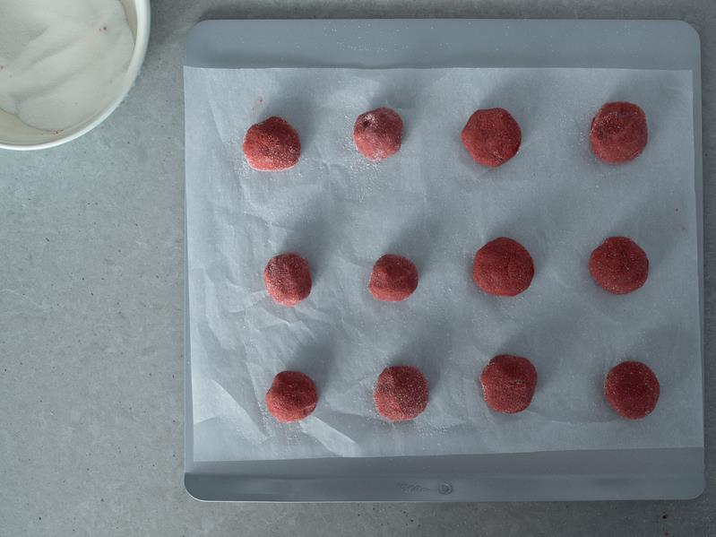 na formie do pieczenia ciastek marki wilton wyłożonej papierem do pieczenia ułożone kulki ciasta na ciasteczka red velvet obtoczone w cukrze