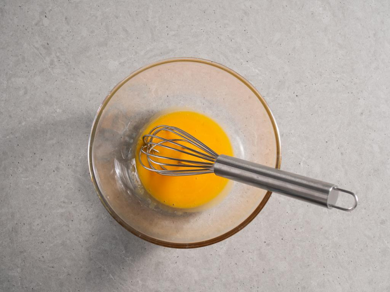szklana miska z rozmieszanymi żółtkami i rózgą kuchenną