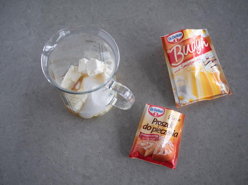 na blacie wysokie naczynie z dodanym twarogiem i cukrem, obok budyń śmietankowy dr. oetkera i proszek do pieczenia dr. oetkera