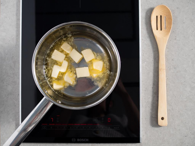 masło, woda i sól na ciasto parzone w rondlu na palniku kuchenki, obok drewniana łyżka