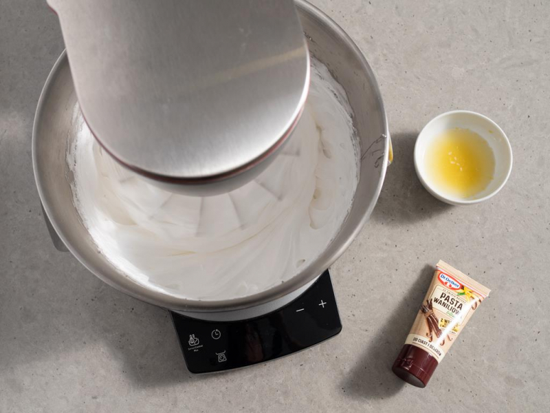 bezowa pianka w misie robota bosch, obok na blacie pasta waniliowa od dr. oetkera oraz sok i skórka z cytryny w miseczce