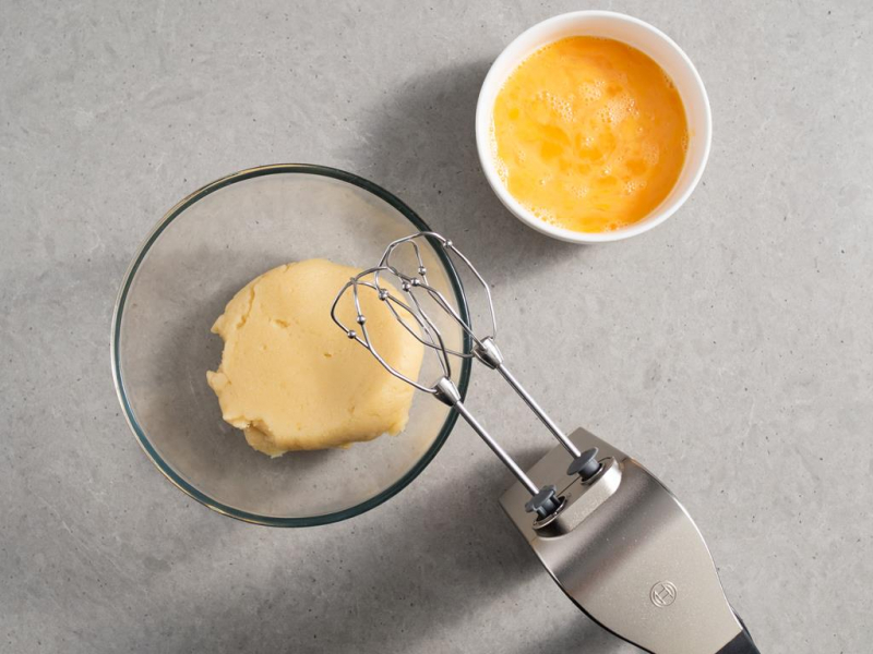 ciasto parzone w szklanej misce, obok w miseczce jajka rozmieszane z białkami oraz mikser ręczny Bosch