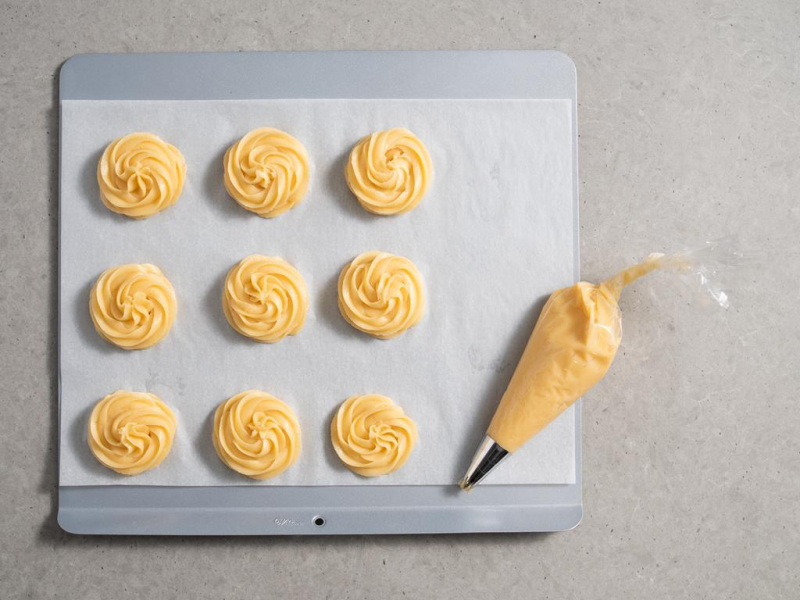 formowanie ptysiów na wentylowanej blasze do pieczenia ciastek marki wilton za pomocą worka cukierniczego z ozdobną tylką marki wilton