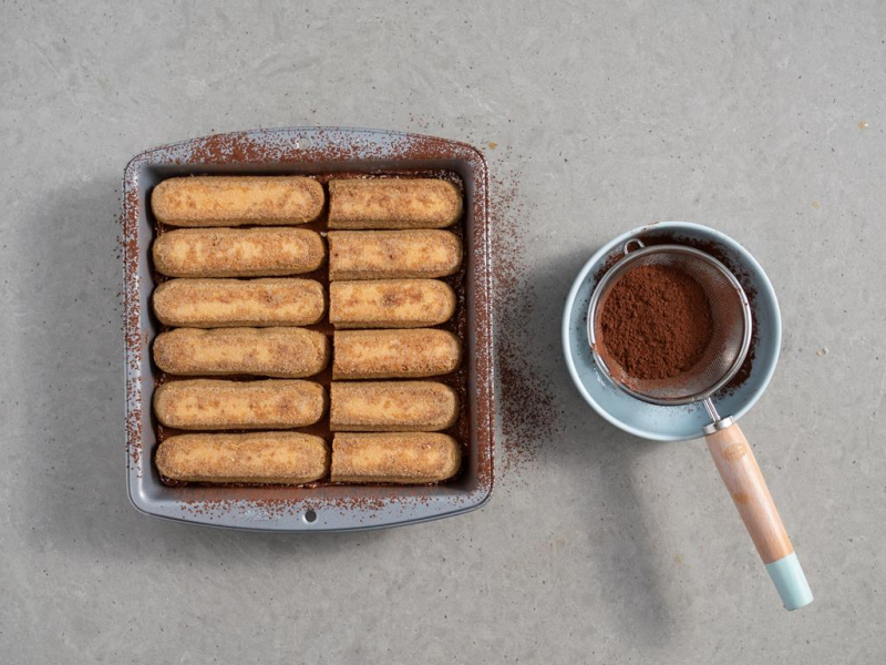 druga warstwa biszkoptów nasączona kawą i ułożona na kremie z likierem baileys, obok sitko z kakao