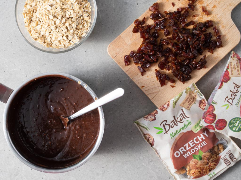 W garnku wymieszana masa czekoladowo-orzechowa. Obok w miseczce płatki owsiane, a na desce acerola i orzechy włoskie.