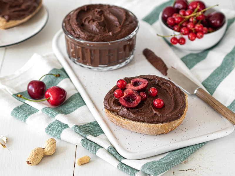 bułka posmarowana cieciorellą czekoladowo-orzechową, obok miseczka z czereśniami i czerwoną porzeczką