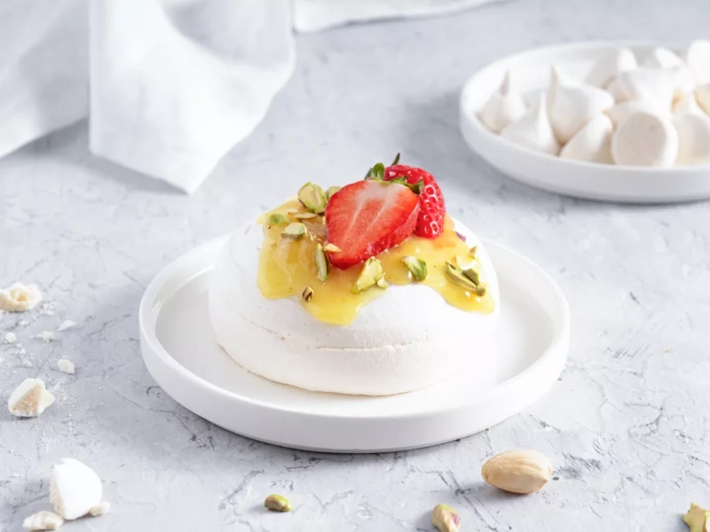 mini beza z lemon curd, świeżymi truskawkami i posiekanymi pistacjami, w tle mini beziki na talerzyku