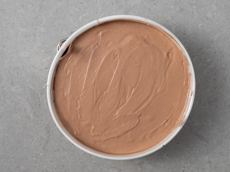 Rozsmarowany w tortownicy ubity krem czekoladowy.