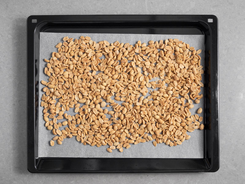 Orzeszki ziemne rozłożone na blasze z wyposażenia piekarnika wyłożonej papierem do pieczenia