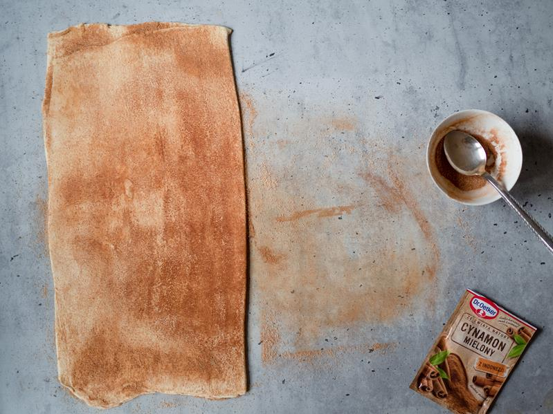 na blacie rozwałkowane ciasto francuskie posypane cukrem z cynamonem, obok opakowanie cynamonu Dr. Oetkera oraz miseczka z cukrem i cynamonem