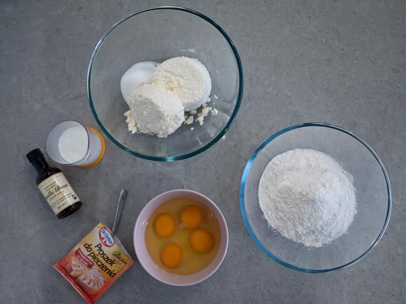 składniki na pączusie: w szklanej misce ser typu włoskiego i cukier, w drugiej szklanej misce mąka pszenna, w małej miseczce 4 jajka, opakowanie proszku do pieczenia dr. oetkera, opakowanie ekstraktu waniliowego taylor&colledge oraz szklana miarka kuchenna z mlekiem