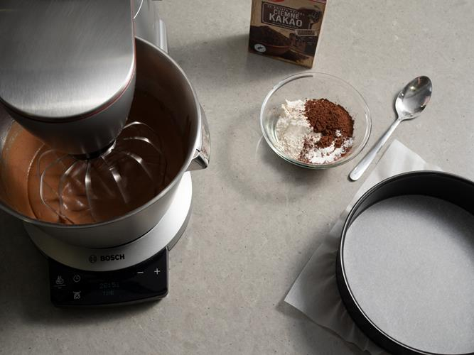 w robocie bosch ubijany krem czekoladowy obok tortownica wyłożona papierem do pieczenia dr. Oetkera