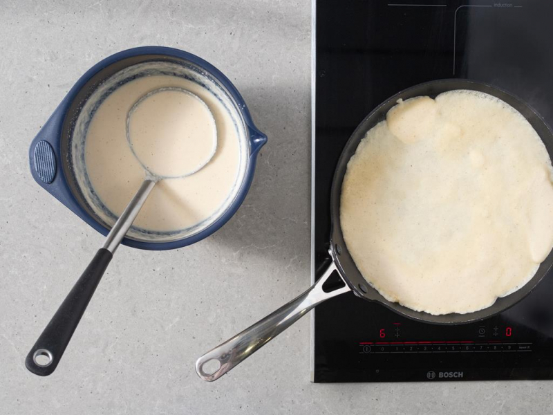 Ciasto naleśnikowe w misce. Obok smażenia naleśnika na patelni.