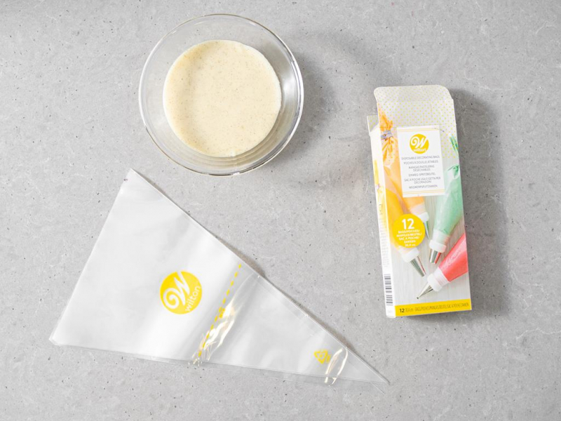 Krem budyniowy w szklanej miseczce. Obok rękaw cukierniczy firmy Wilton.