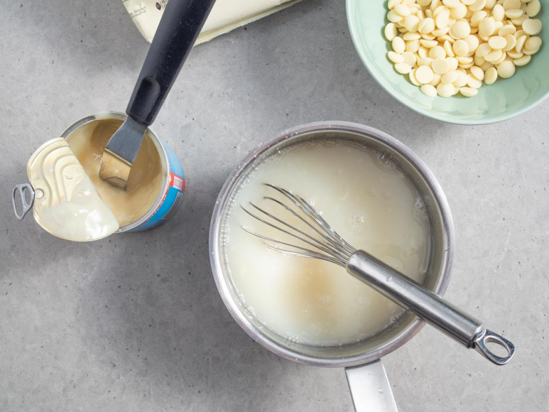 rondel z masą na glazurę obok mleko skondensowane i kaletki czekolady Callebaut