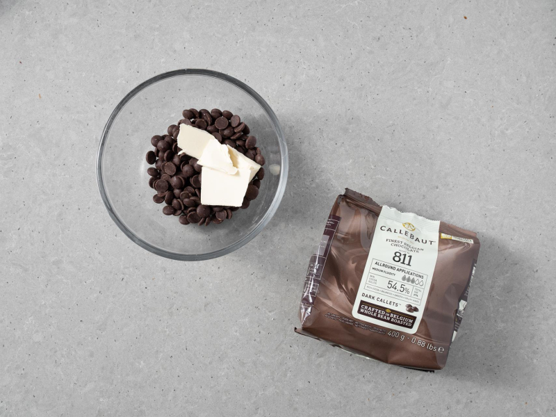 W misce czekoladowe kaletki z masłem roślinnym. Obok na blacie opakowanie czekolady callebaut 811.