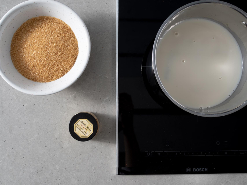 W garnku napój migdałowy. Obok cukier trzcinowy w misce i opakowanie pasty z wanilii Taylor&Colledge.