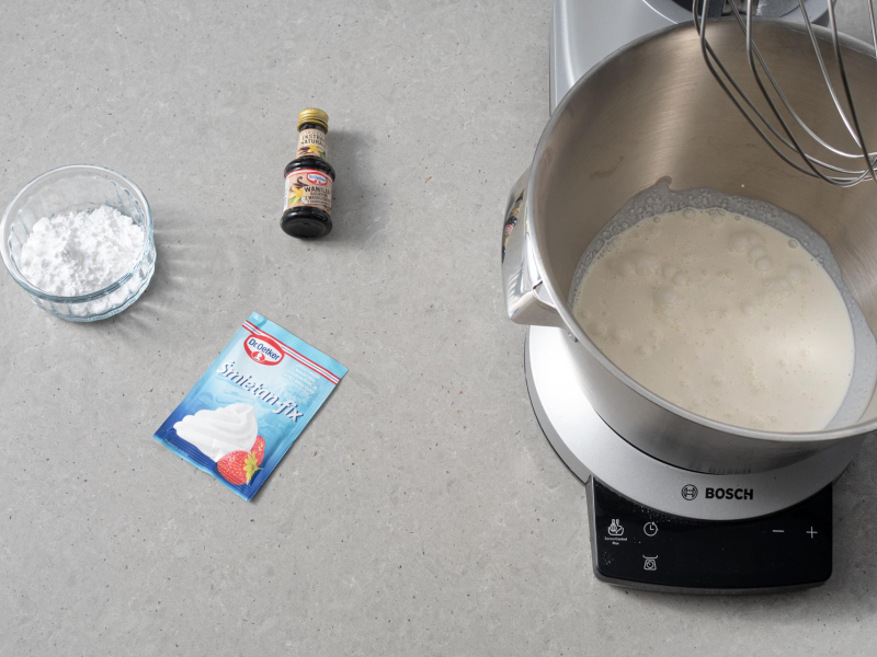 W misie robota kuchennego sch艂odzona 艣mietanka. Obok 艣mietan-fix i ekstrakt z wanilii, a obok cukier puder w miseczce.