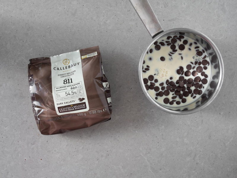 Na blacie opakowanie czekolady ciemnej Callebaut 811 oraz garnek z czekoladą i napojem sojowym.