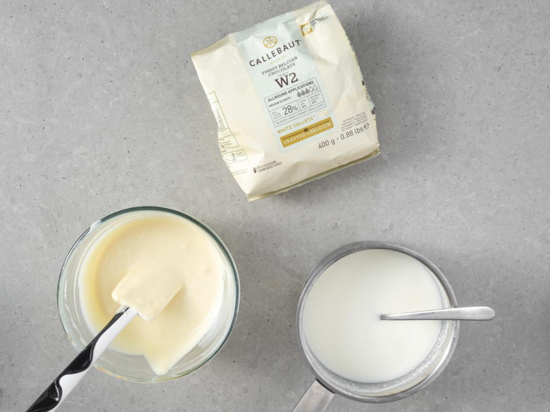 Na blacie opakowanie białej czekolady callebaut w2. W misce rozpuszczona czekolada, a obok masa jogurtowa.