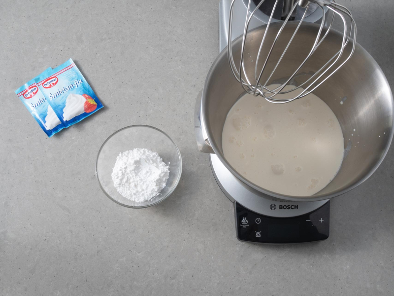 W misie miksera śmietanka. Obok 2 opakowania śmietan fix i cukier puder w miseczce.