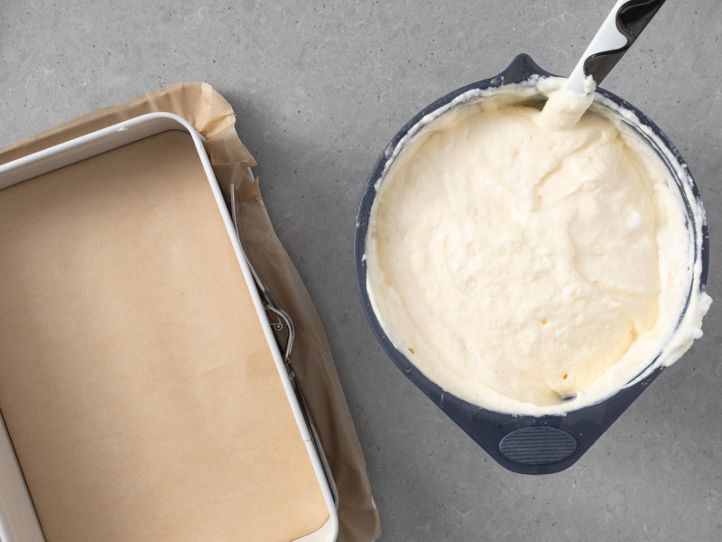 Prostokątna forma wyłożona papierem do pieczenia. Obok w misie wymieszana masa na skyrnik.