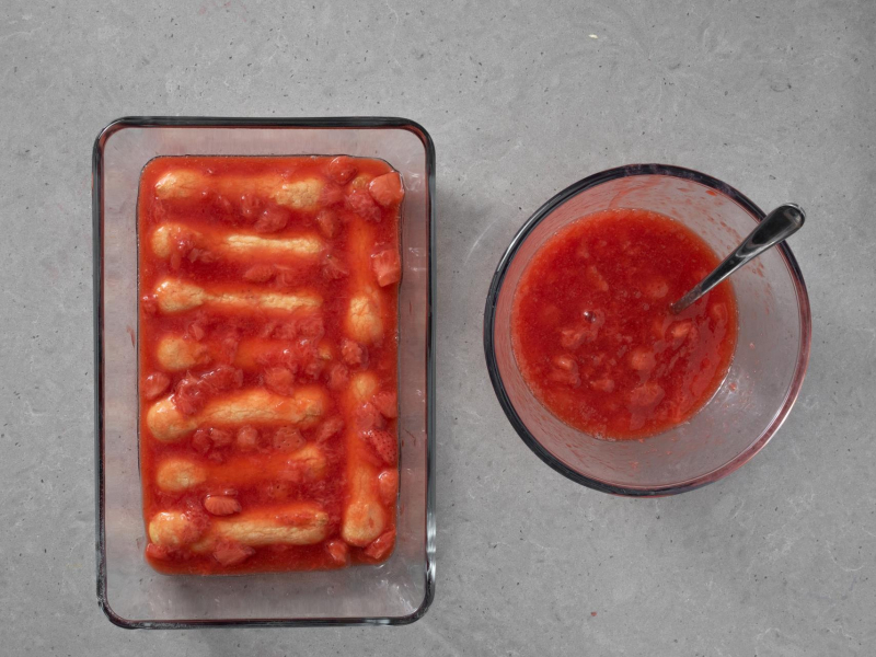 W misce mus truskawkowy. W szklanej formie wyłożone biszkopty, przykryte owocami.