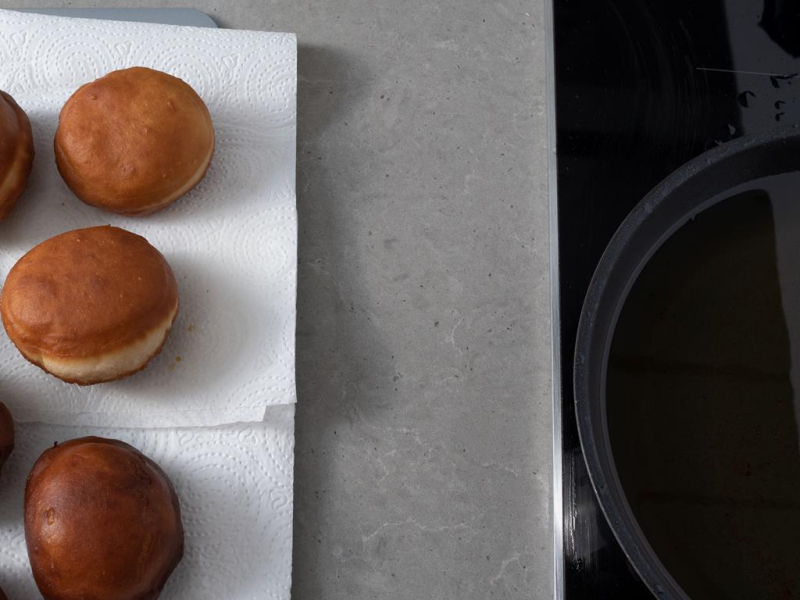 Usmażone pączki bez mleka. Obok patelnia na płycie indukcyjnej.