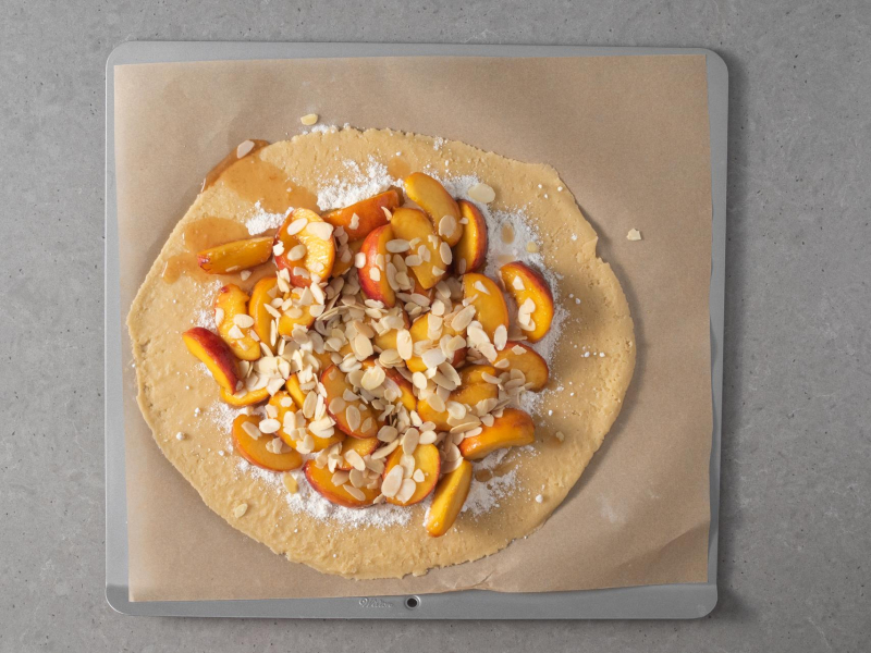 Rozwałkowane ciasto kruche z brzoskwiniami i płatkami migdałów.