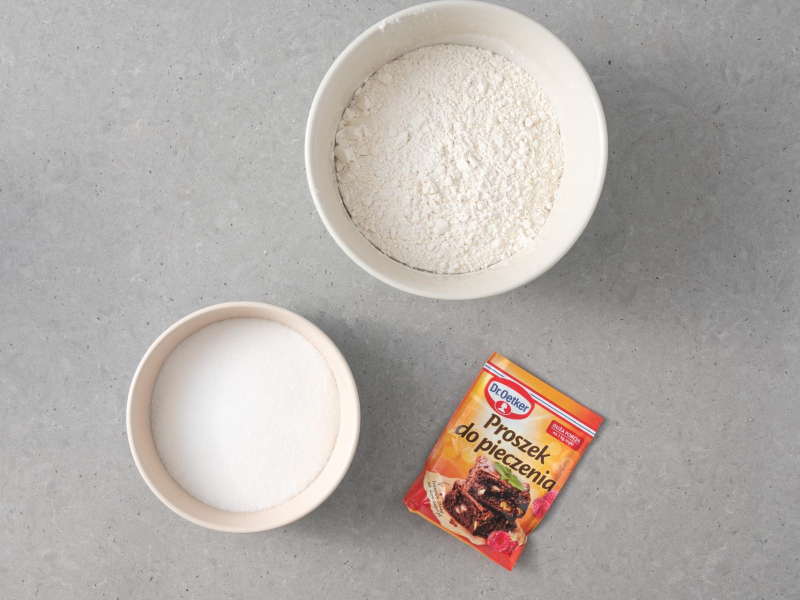 W miseczce mąka, obok cukier i na blacie proszek do pieczenia Dr. Oetkera.