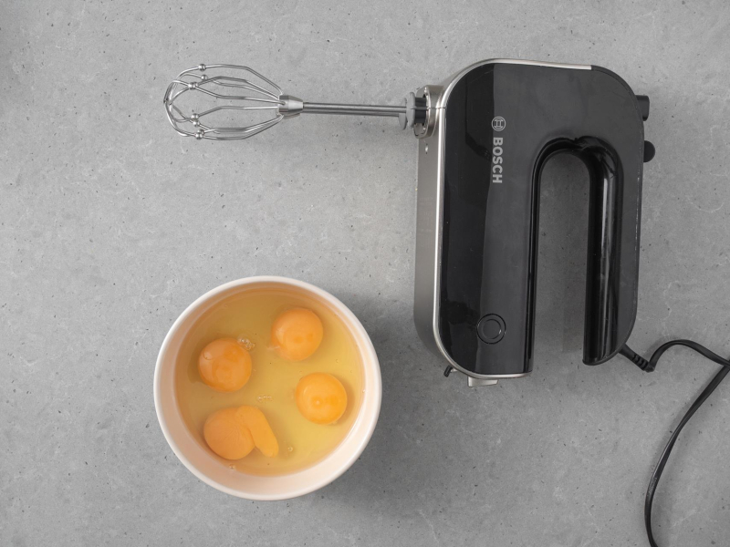 Na blacie kuchennym robot ręczny Bosch. Obok jajka w misce.