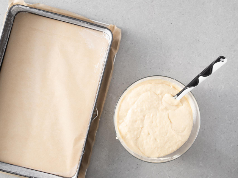 Forma do pieczenia wyłożona papierem do pieczenia. Obok wymieszane ciasto w misce.