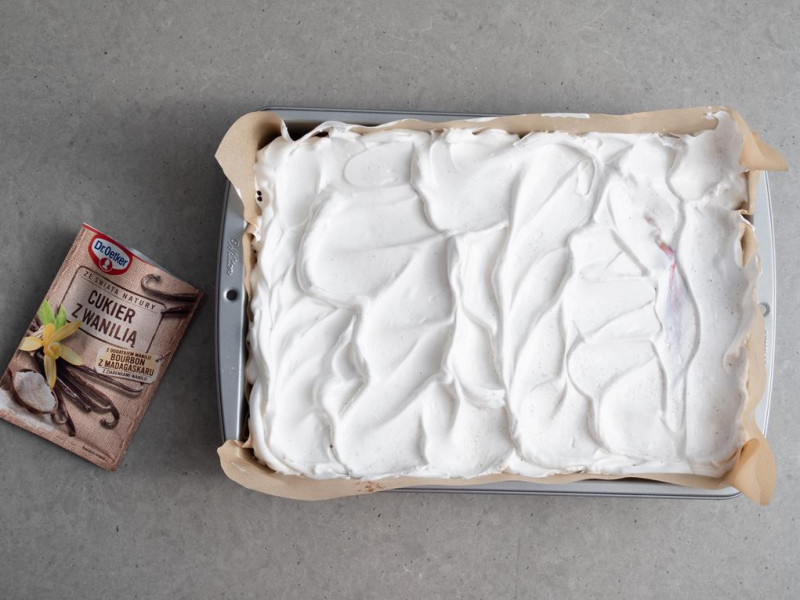 w formie do pieczeni ciasto z warstwą bezy u góry obok cukier z wanilią dr. oetkera