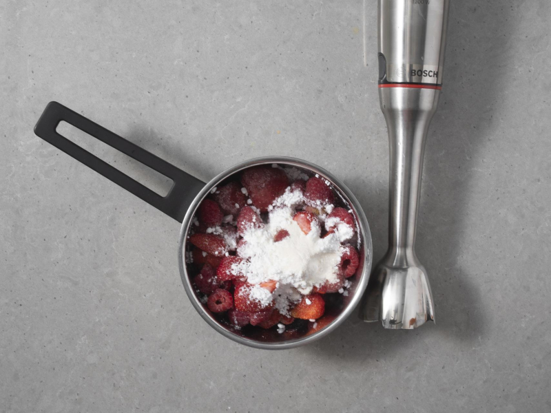 W garnku sezonowe owoce razem z cukrem pudrem i agarem. Obok blender firmy Bosch.