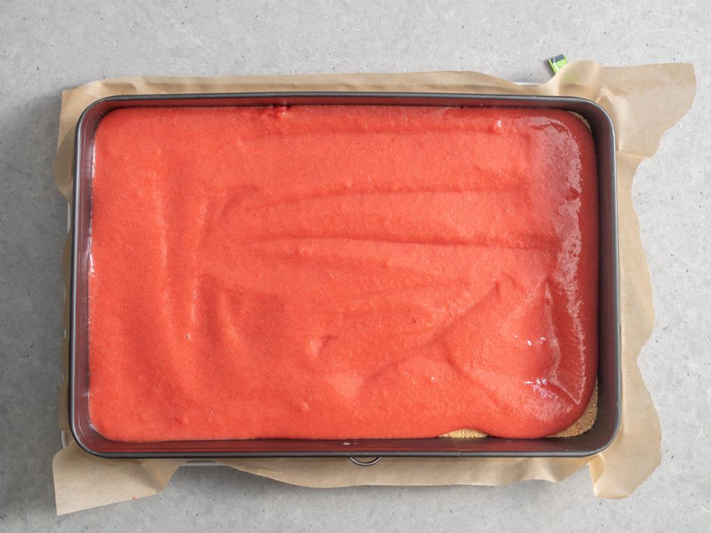 w prostokątnej formie do pieczenia ciasto z warstwą gładkiego dżemu truskawkowego