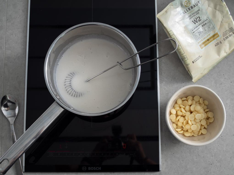 w rondelku na płycie indukcyjne bosch mleczko kokosowe obok w miseczce blała czekolada w kaletkach Callebaut