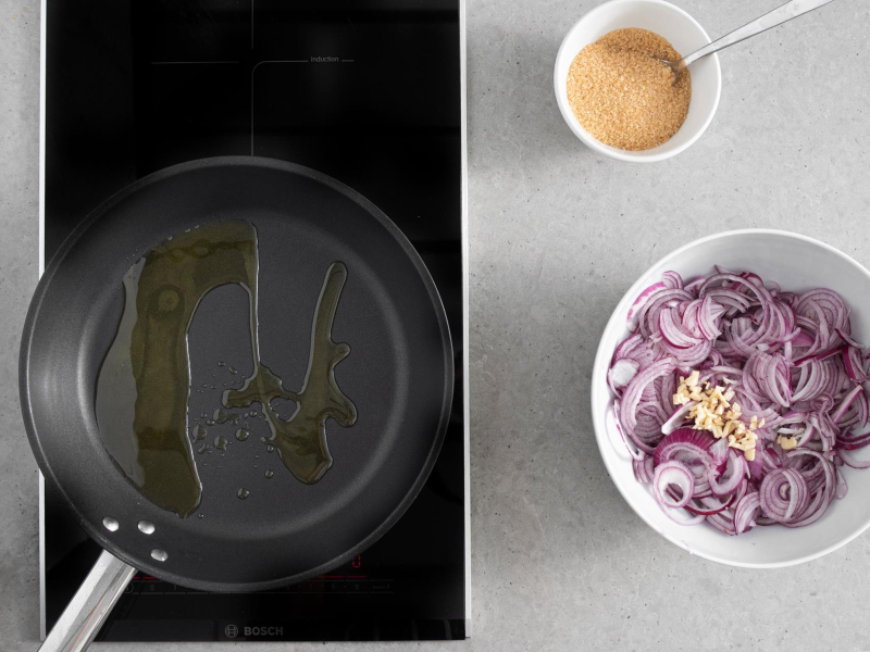 Na patelni rozgrzana oliwa. Obok w misie czerwona cebula i cukier trzcinowy.