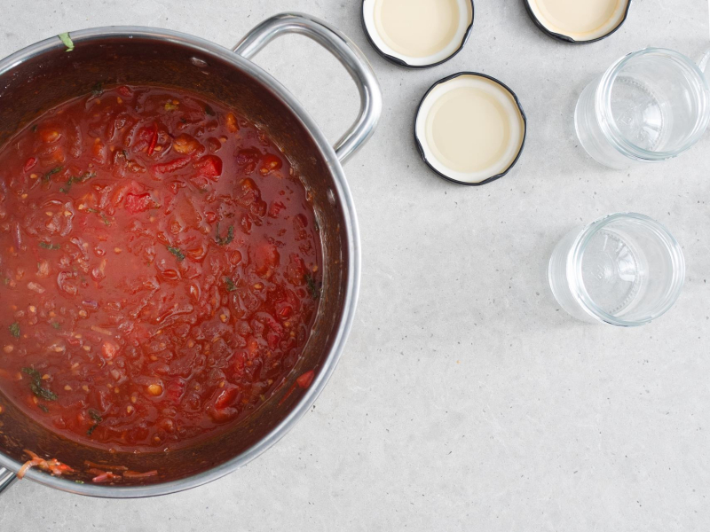 W garnku gotowy chutney z pomidorów i czerwonej cebuli. Obok przygotowane słoiczki.