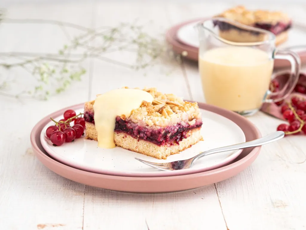 Kawałek  kruchego ciasta z czerwonymi owocami i kruszonką na talerzyku z sosem waniliowym- Wszystkiego Słodkiego