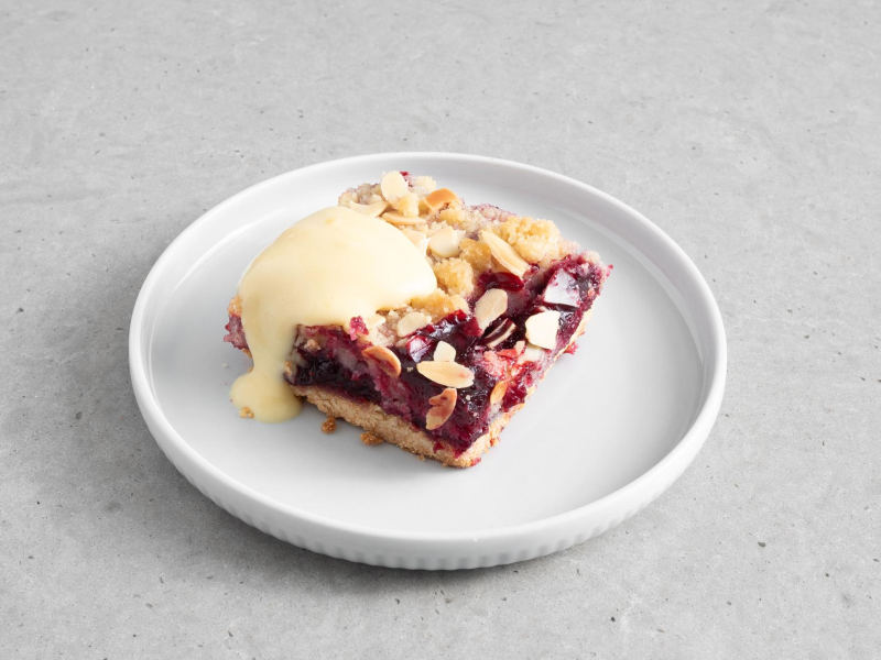 Kawałek ciasta kruchego z owocami i kruszonką oraz sosem waniliowym.