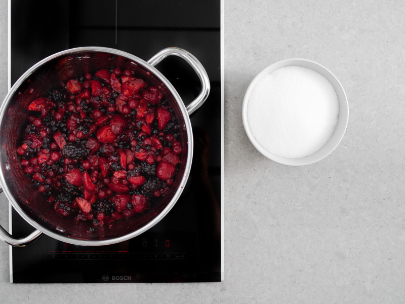 Zagotowane owoce z żelfixem w garnku. Obok cukier w miseczce.