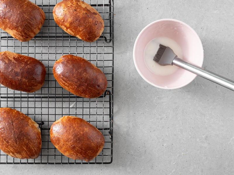 Upieczone jagodzianki na kratce do studzenia. Obok miseczka z lukrem.
