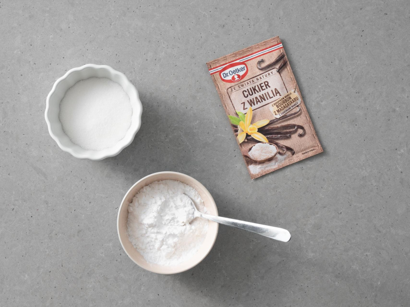 Na blacie kuchennym cukier z wanilią Dr. Oetkera. Obok cukier w miseczce oraz mąka ziemniaczana.