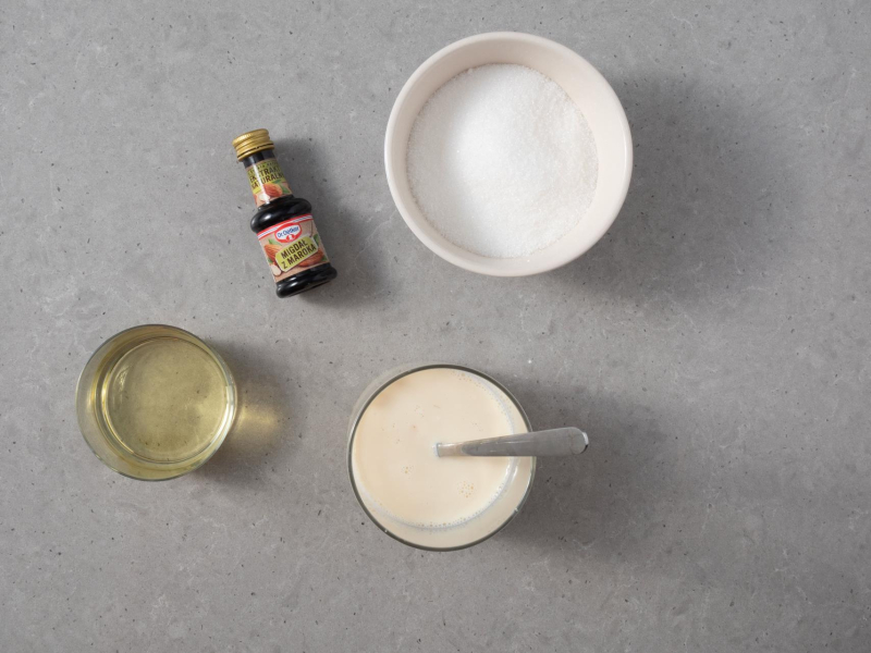 Na blacie kuchennym olej rzepakowy w misce, cukier, napój sojowy z octem oraz ekstrakt migdałowy Dr. Oetkera.