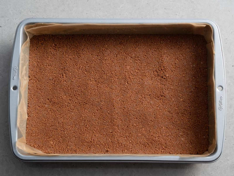 prostokątna forma wyłożona papierem do pieczenia i ze spodem z ciasteczek kakaowych